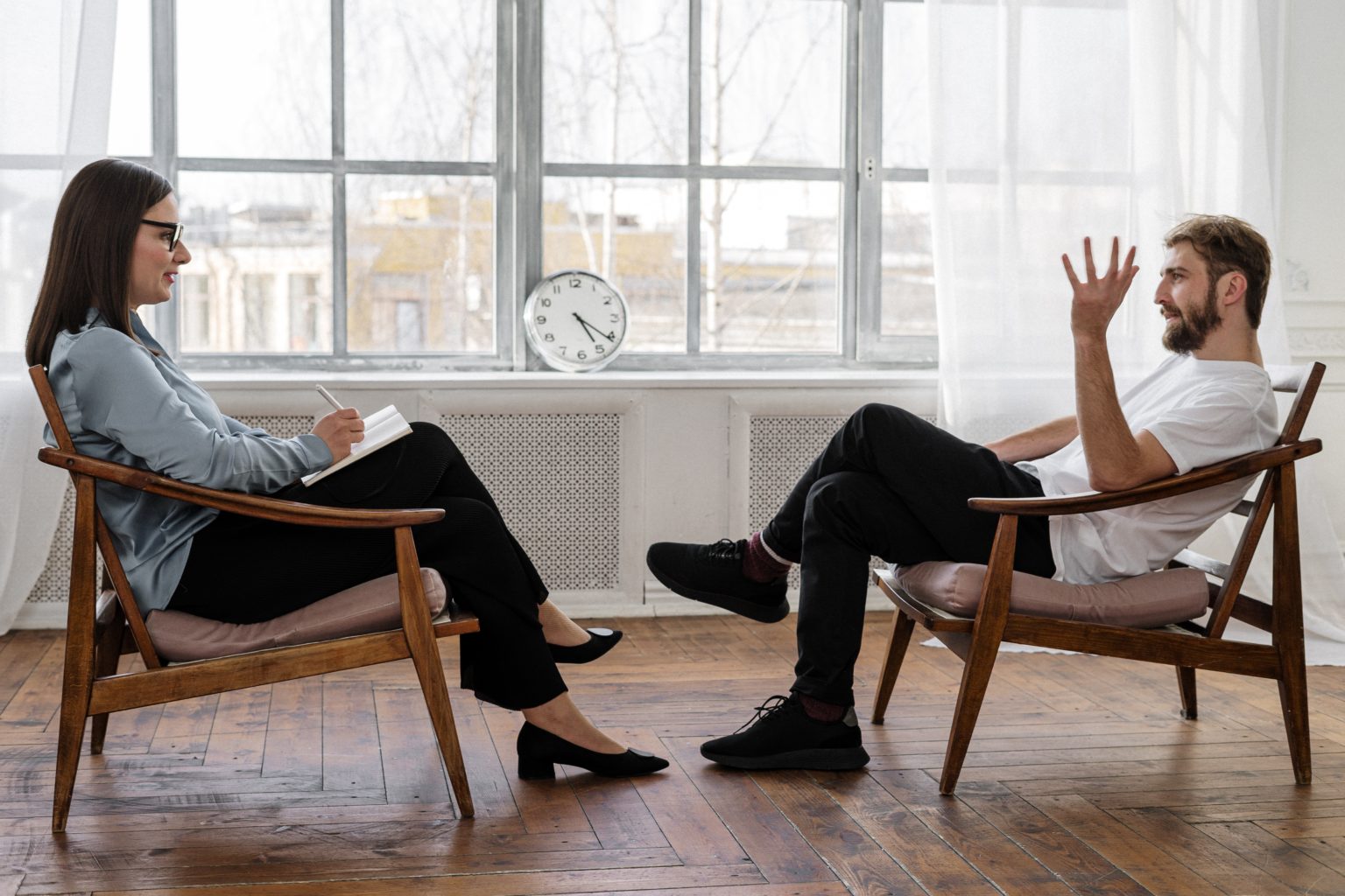 a man and a woman sitting in chairs in a room with a clock