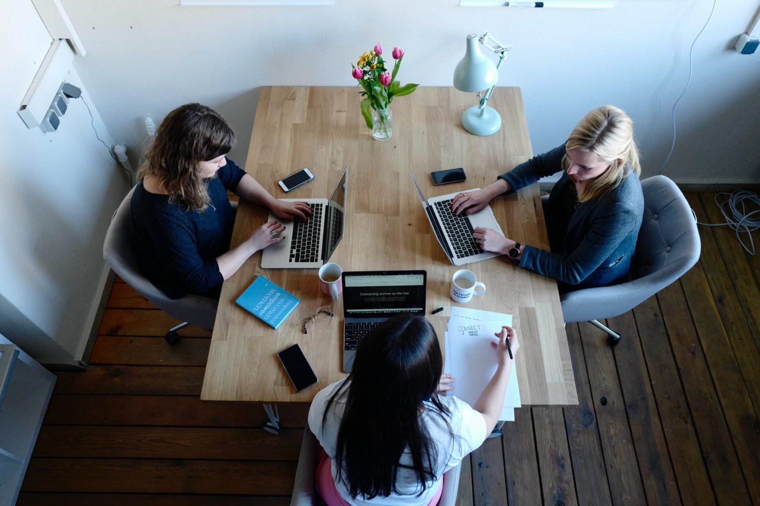 a group of women sitting at a table working on laptops